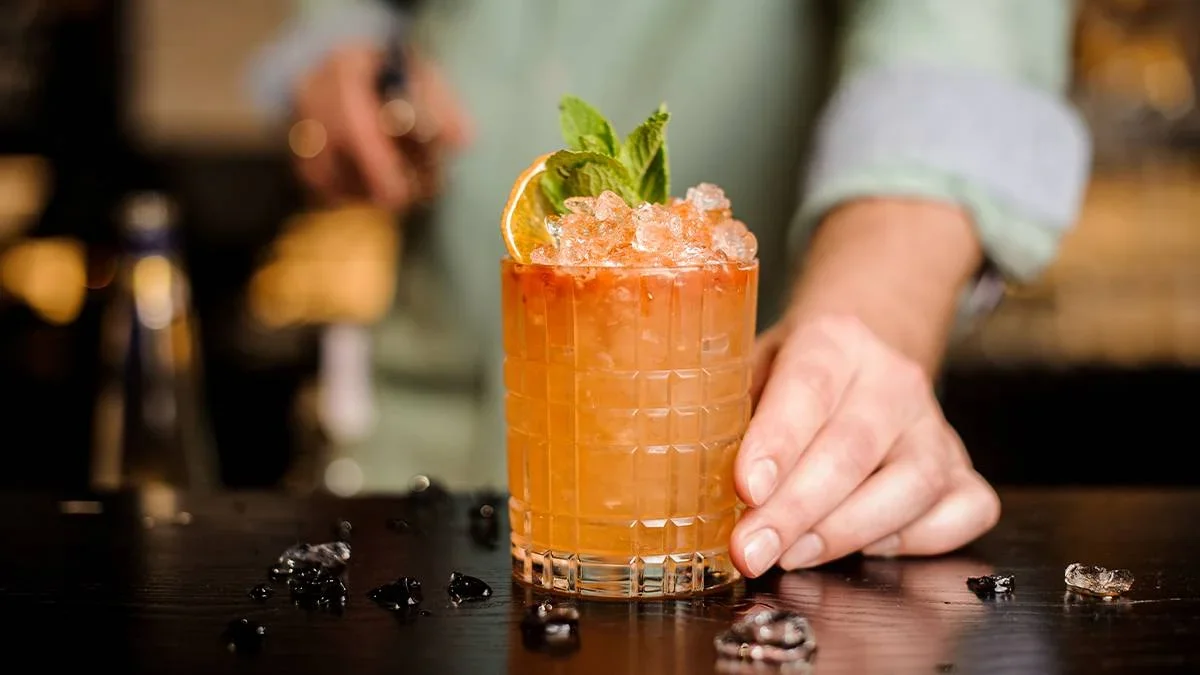 Bartender setting a mixed drink with fruit and mint garnish down on the bar.